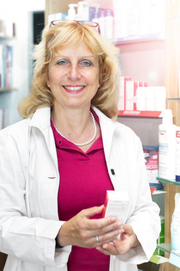 Caren Caren Ahnefeld (Apothekerin) hält eine Medikamentenpackung in den Händen. Im Hintergrund sind Verkaufsregale zu sehen.