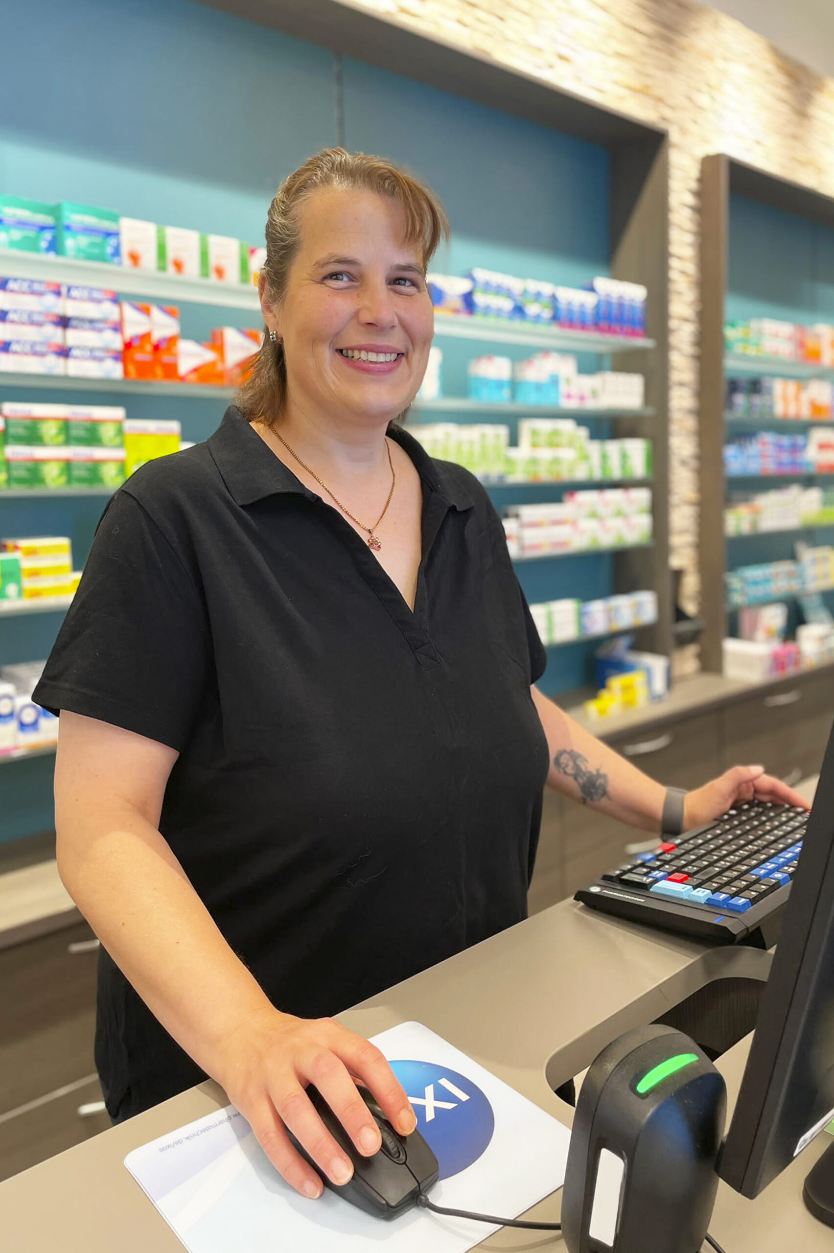 Katja Katja Ledl steht hinter dem Tresen am Computer und lächelt in die Kamera.
