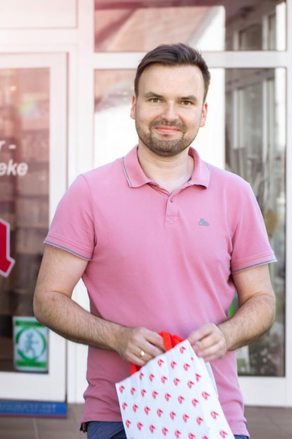 Matthias Matthias Mengel steht vor dem Eingang der Apotheke und hält eine weiß-rote Tragetasche in den Händen.