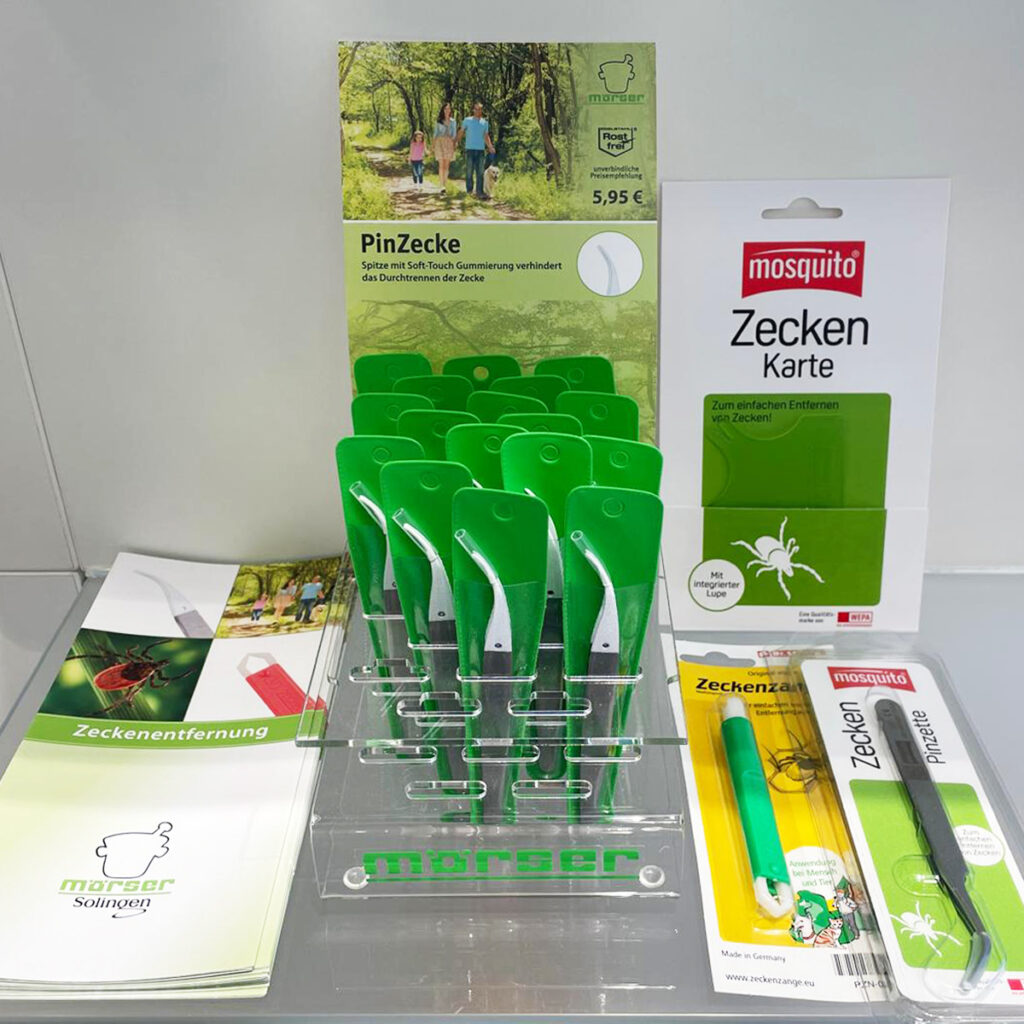 Ein Verkaufstresen in einer Apotheke mit einem Display-Ständer für grüne Zeckenpinzetten sowie verschiedenen Informationsbroschüren, Zeckenkarten und Zeckenzangen zur sicheren Parasitenentfernung.